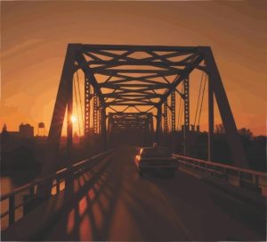 A cruiser drives on one of the many bridges over the South Saskatchewan at the sun creeps up on the prairies.
